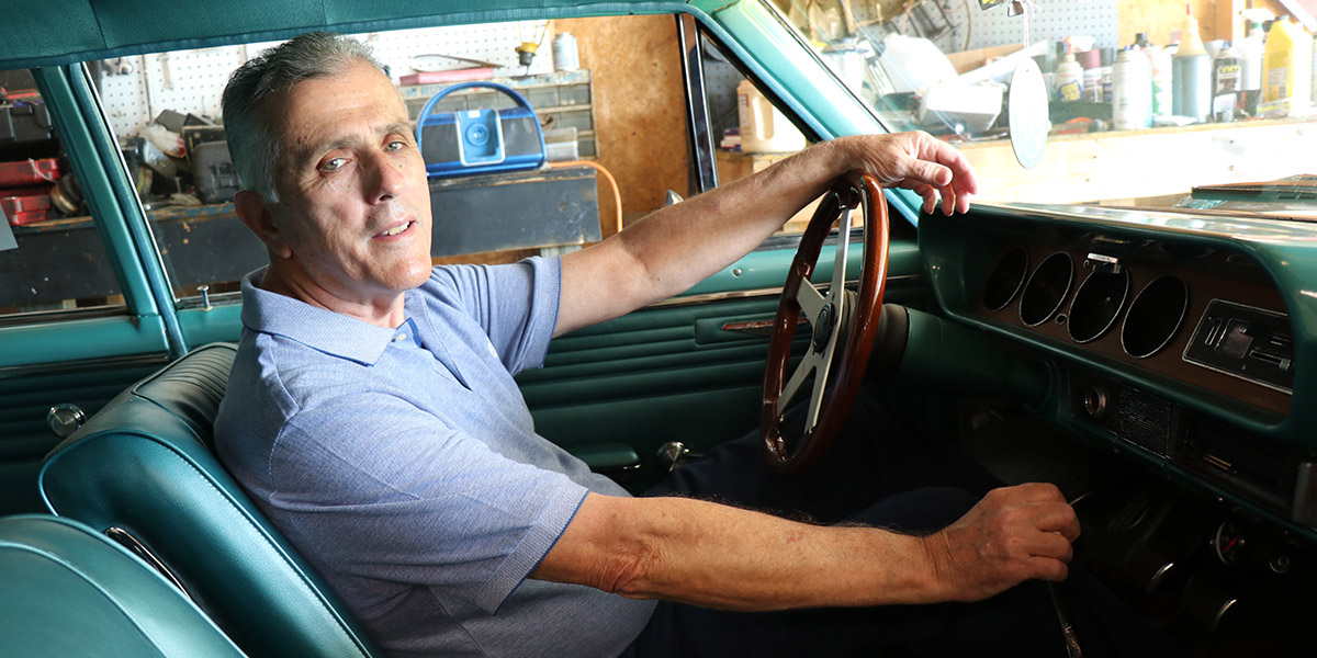 David Adkins, apatient who underwent the MitraClip procedure, sits in front of the steering wheel in a classic car