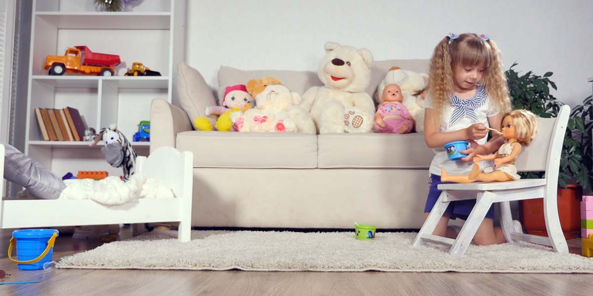Little girl in a child's playroom filled with toys, feeding a babydoll