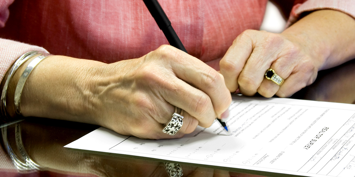  Mature woman's hands are signing end-of-life planning forms and documents