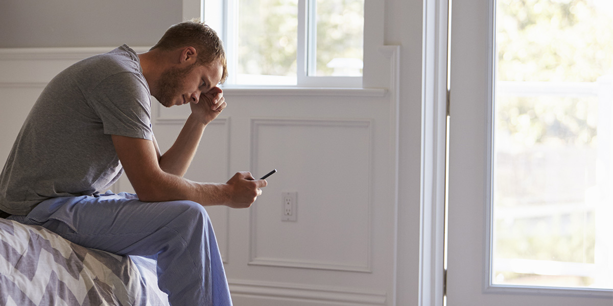 Stressed Man Wearing Pajamas Using Mobile Phone In Bedroom